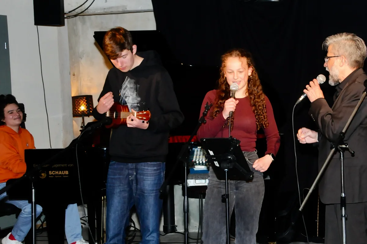 Man sieht Musikerinnen und Musiker auf der Bühne spielen und singen.